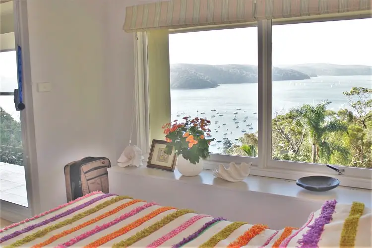 A bed and view of a lake from the window at a luxury house sit in Sydney.