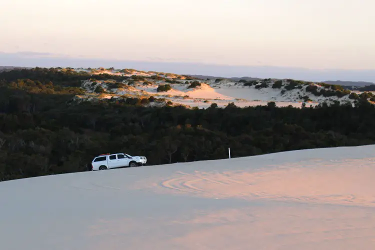 A 4WD heading up a sand dune at sunset in Western Australia.