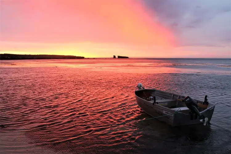 Rowing boat on calm water with a bright red sunset behind in Elliston, South Australia.