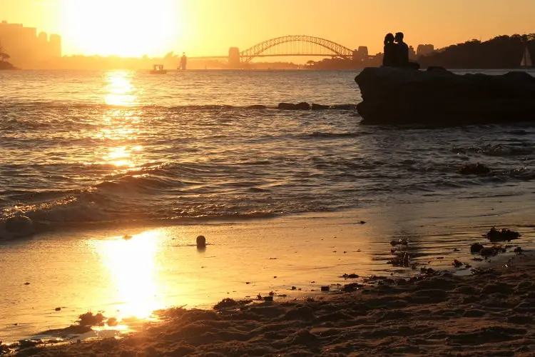 Beautiful orange sunset with Sydney Harbour Bridge across the water, viewed from Milk Beach.