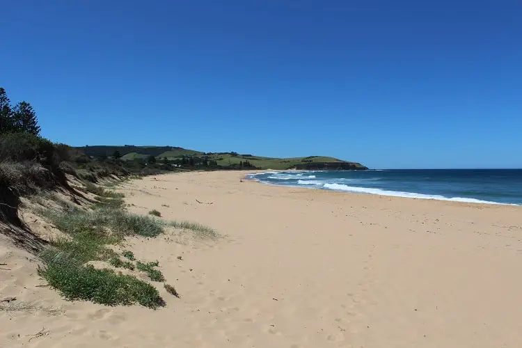 Sunny Werri Beach with green hills behind.