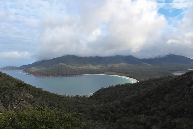 Looking down over Wineglass Bay in Tasmania with low cloud covering the mountaintops.