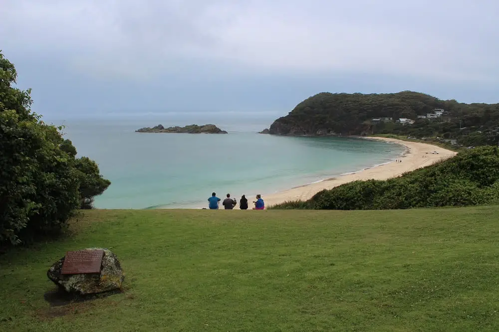 Visitors sitting on the headland at Seal Rocks, overlooking the beach on a cloudy day.