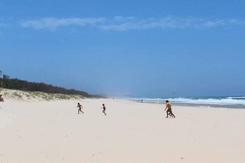 A family running across very white sand at Peregian Beach in the Sunshine Coast, Queensland, a popular holiday destination.
