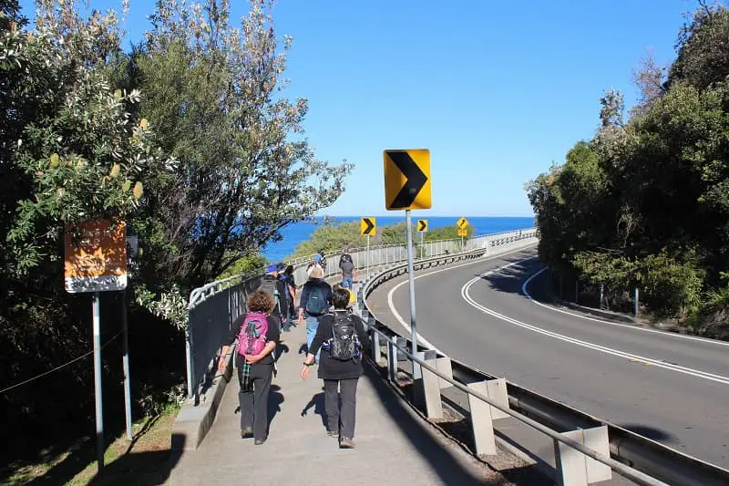 A group of hikers walking across Sea Cliff Bridge in Sydney wintertime.