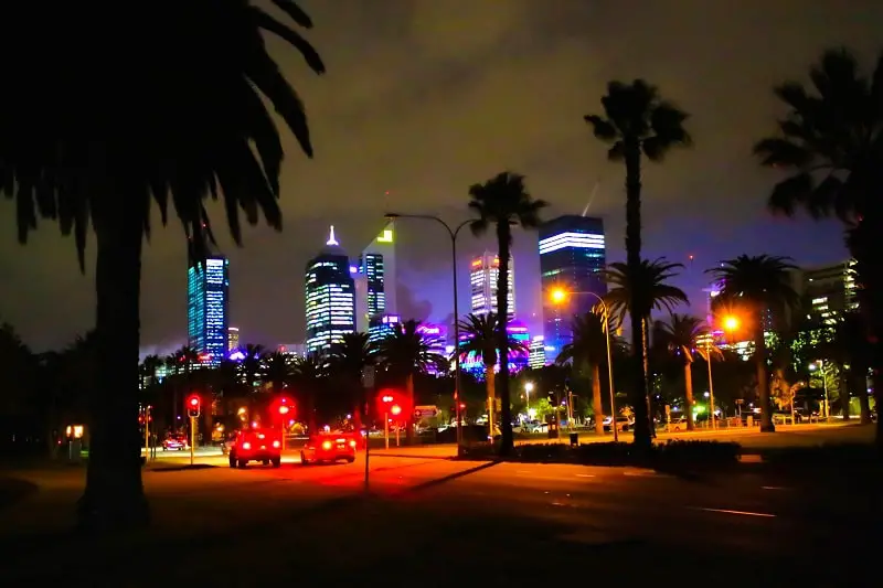 Perth CBD lit up at night with palm trees in front.